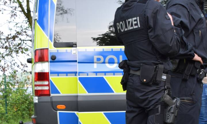 Bewaffnete Polizisten in schwarzer Uniform vor einem Polizeiauto Betrüger wollen Geld für angebliche Notfallbehandlungen